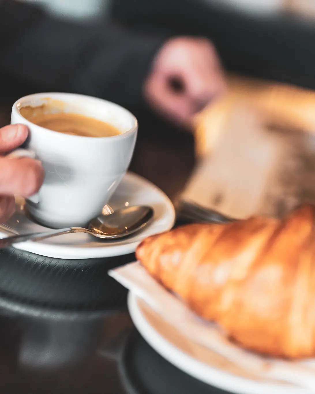 Kaffee und Croissant am Tisch, daneben die Tageszeitung